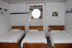 Una habitación con tres camas de madera alineadas, ropa de cama blanca, un ventanal con vistas y una pared con un cuadro.