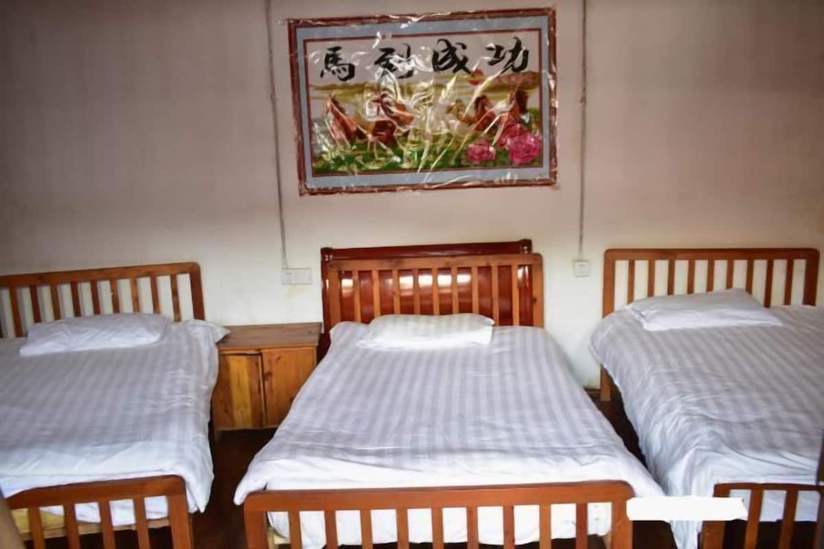 A room with two wooden beds, each with a white mattress and a wooden headboard. There is a wooden nightstand between the beds, and a framed picture hangs on the wall above the beds.
