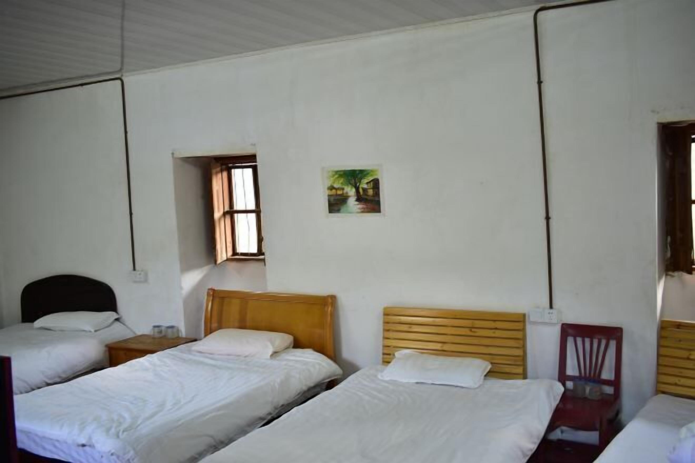 Una habitación con tres camas individuales, una ventana pequeña, un cuadro en la pared y una silla roja.