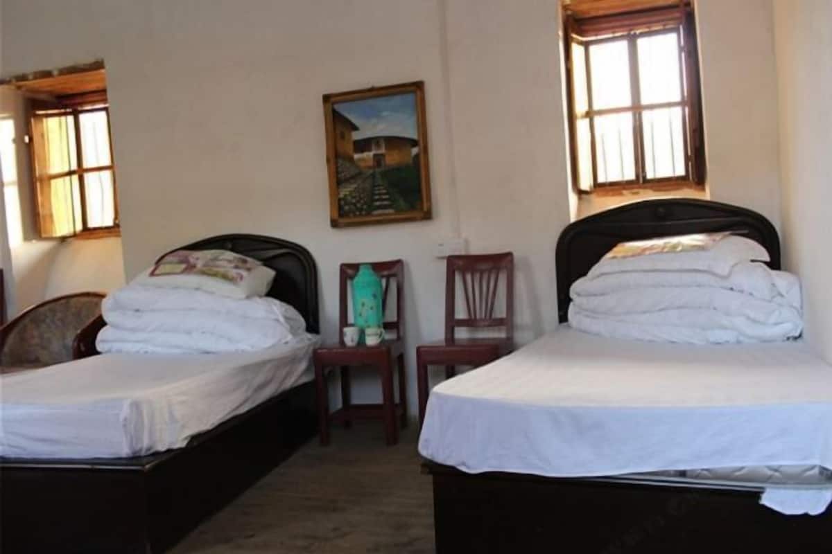 Two single beds with white linens, a small wooden chair, a framed picture on the wall, and a window with wooden shutters.