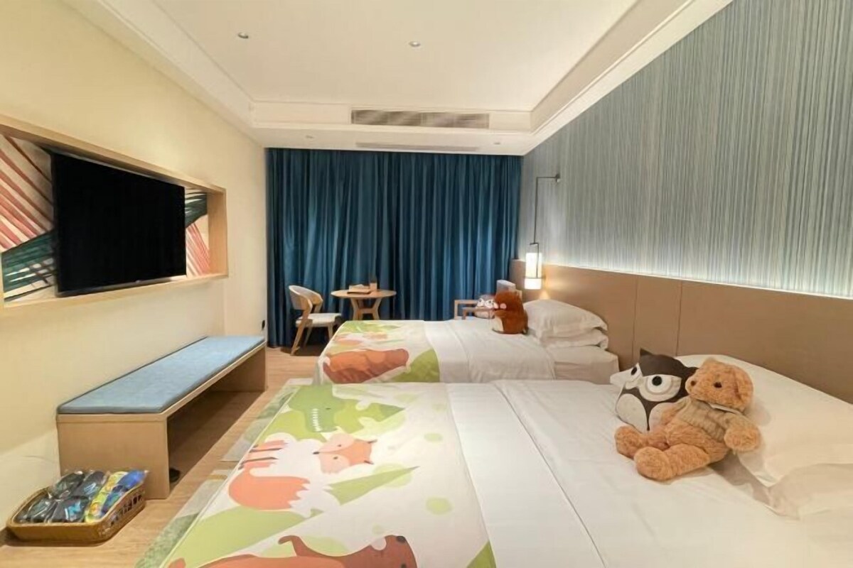 A hotel room with a bed, a bench, a TV, a desk, and a window with curtains.