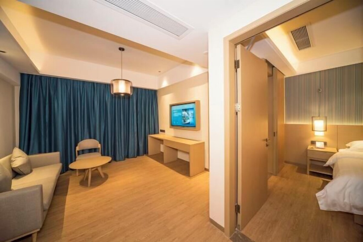 A hotel room with a sofa, a desk, a chair, a TV, and a bed.