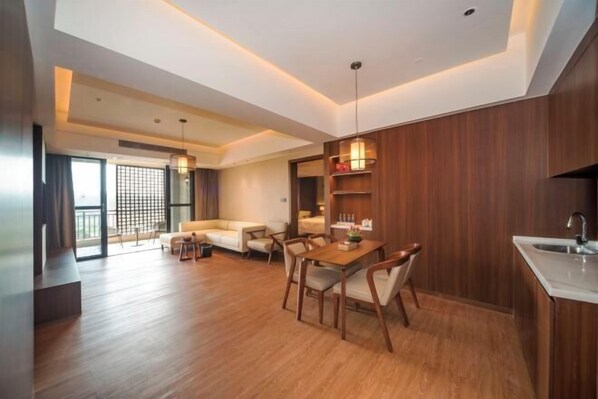 A modern living room with a wooden dining table and chairs, a sofa, and a kitchen area with a sink and cabinets. - Freely Hover Golden Shuitai Hot Spring Town (Xinxing)