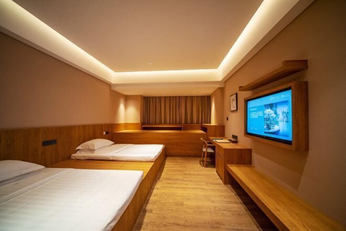 A hotel room with two beds, a desk, a chair, a television, and a large window.