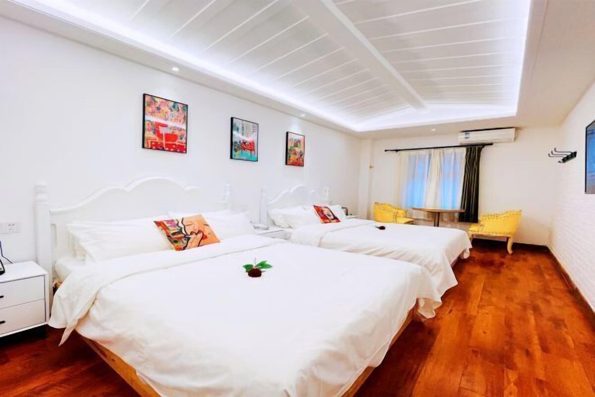 A hotel room with two beds, white bedding, a wooden floor, and artwork on the walls.