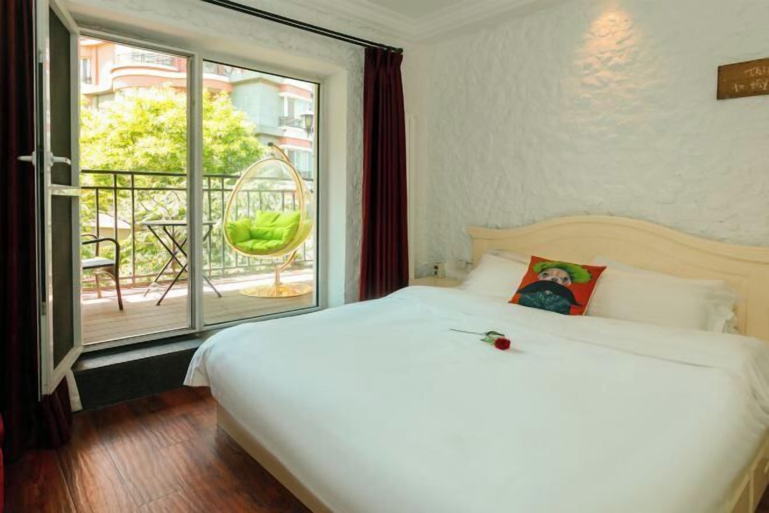 A hotel room with a large bed, a hanging chair by the window, and a view of the outside balcony.