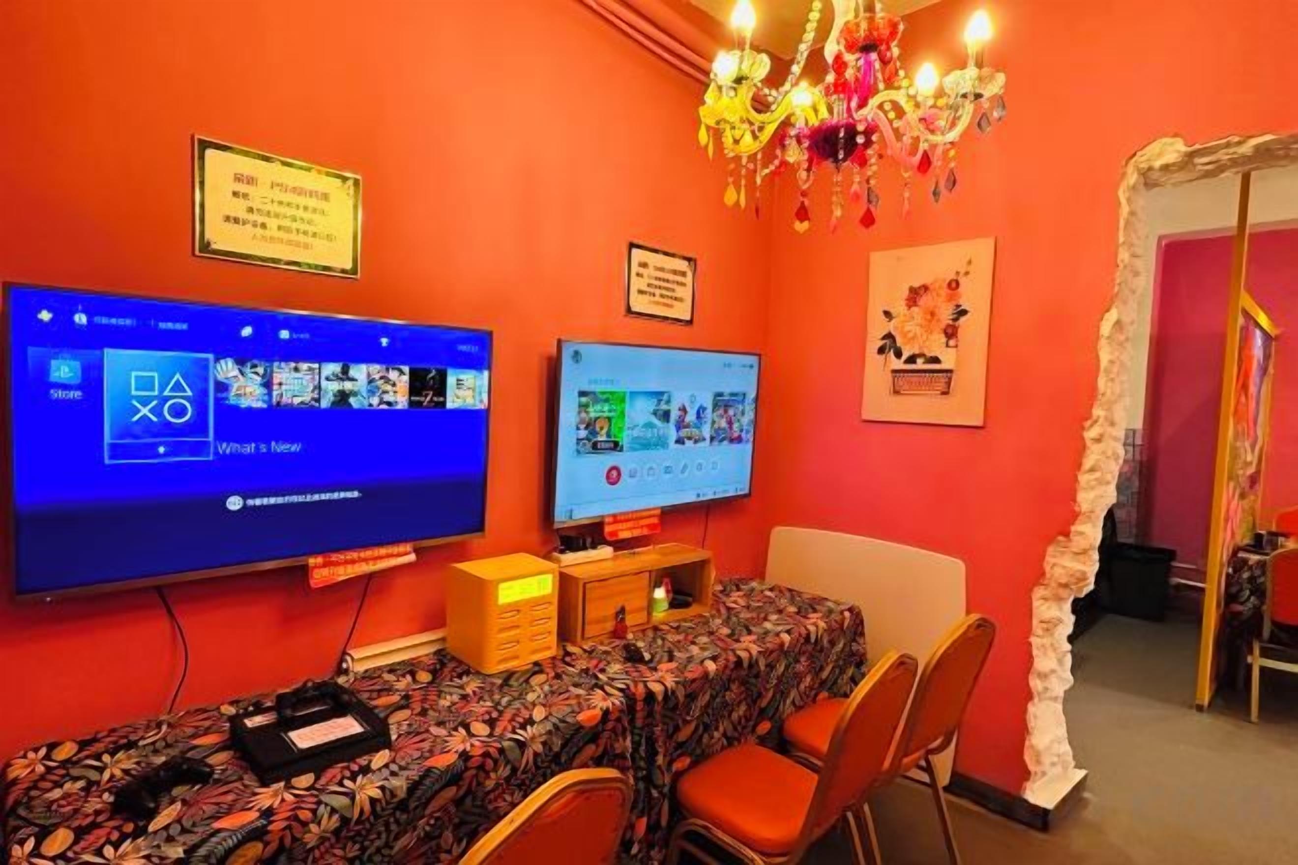 A room with a red wall, a large flat-screen TV, a table with chairs, and a chandelier.
