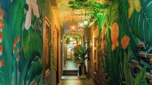 Un pasillo decorado con un mural de plantas y flores tropicales, paredes de ladrillo y luces colgantes.