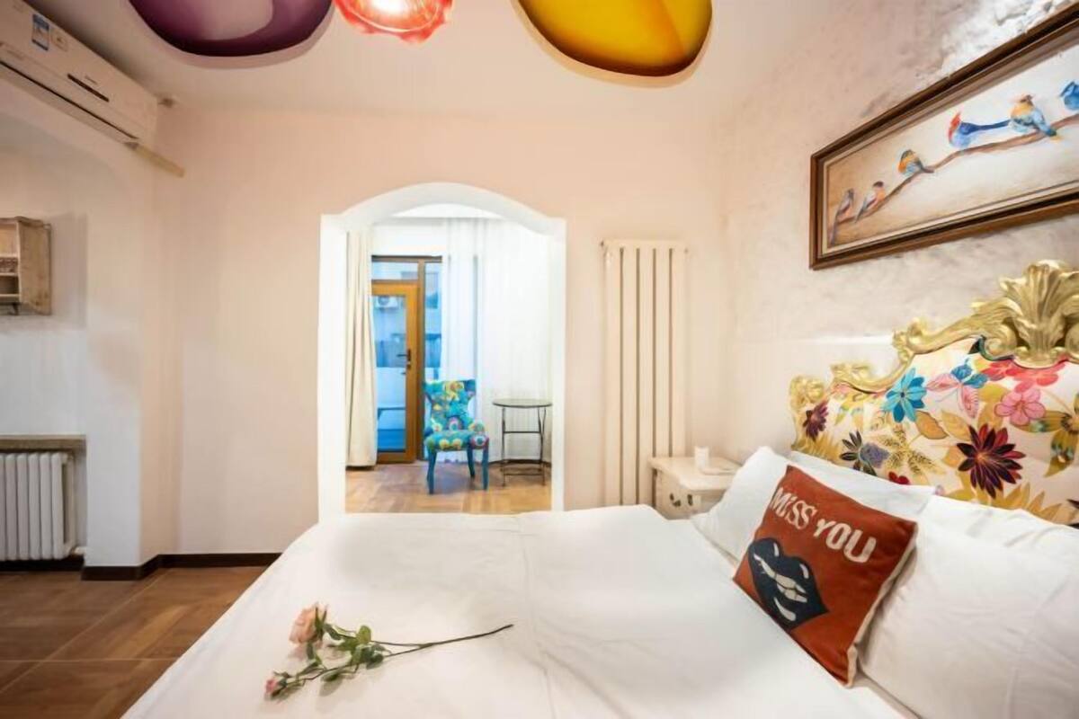 Hotellihuone, jossa on sänky, kukkakuviollinen tyyny, taulu ja näkymä käytävään.