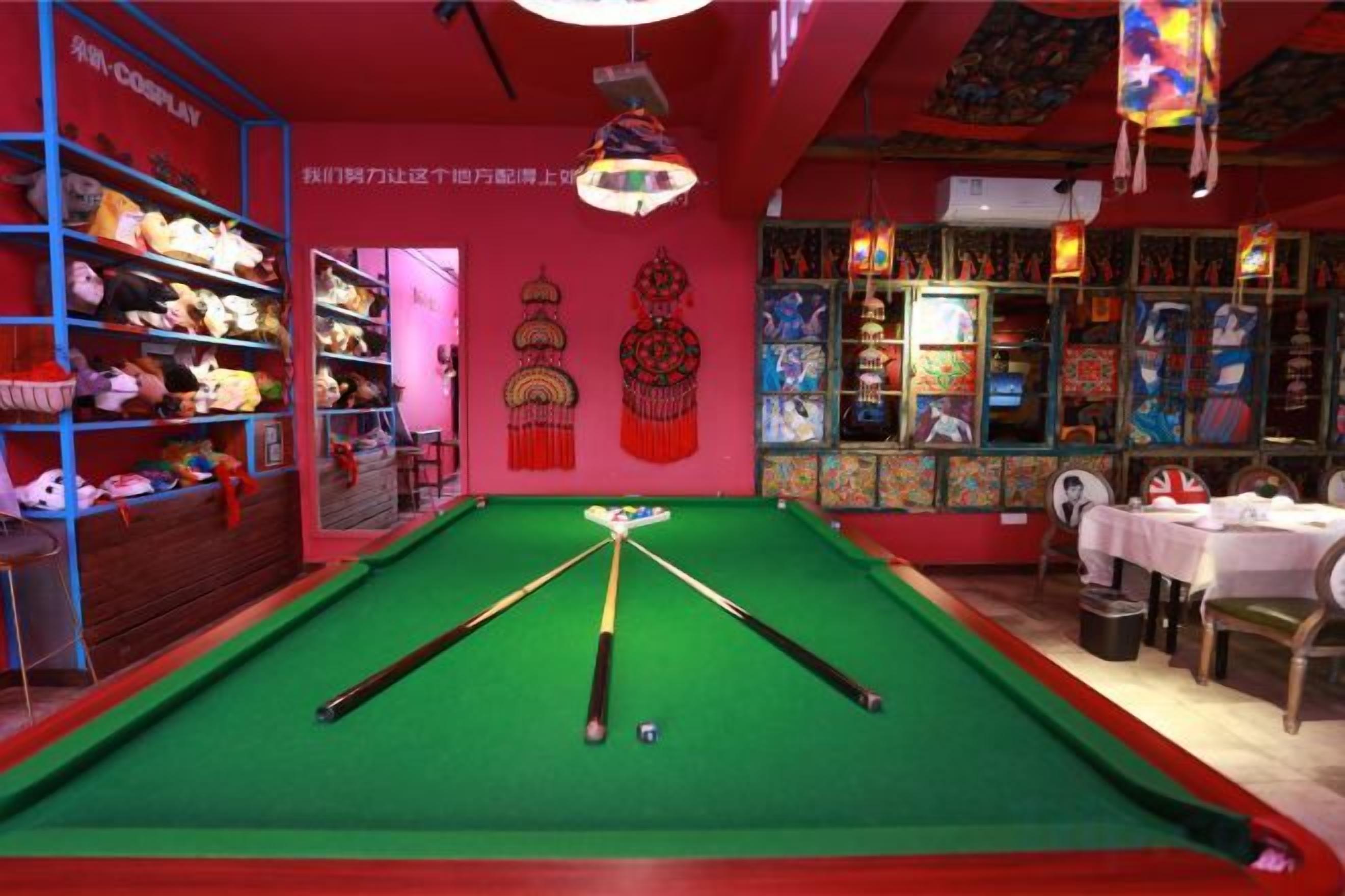 Una sala de billar con mesa de billar, estanterías con peluches y una pared roja con detalles decorativos.