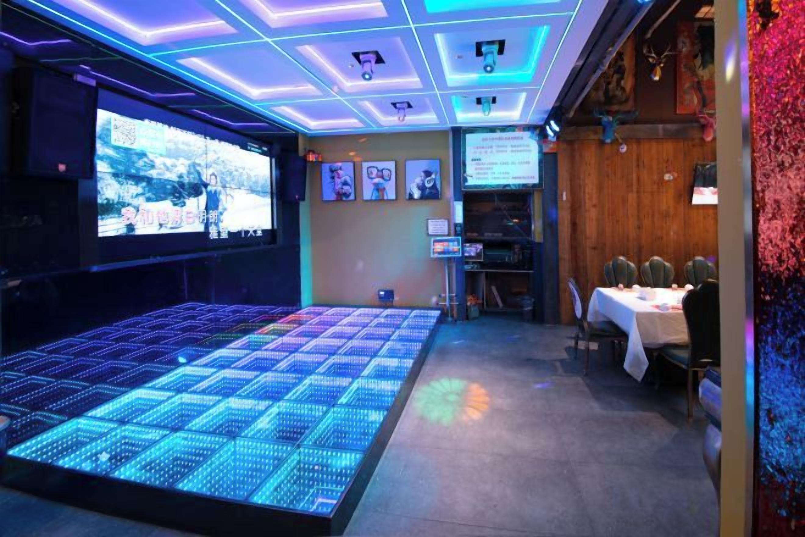 A room with a large LED screen, a seating area with tables, and a wooden wall with a clock.