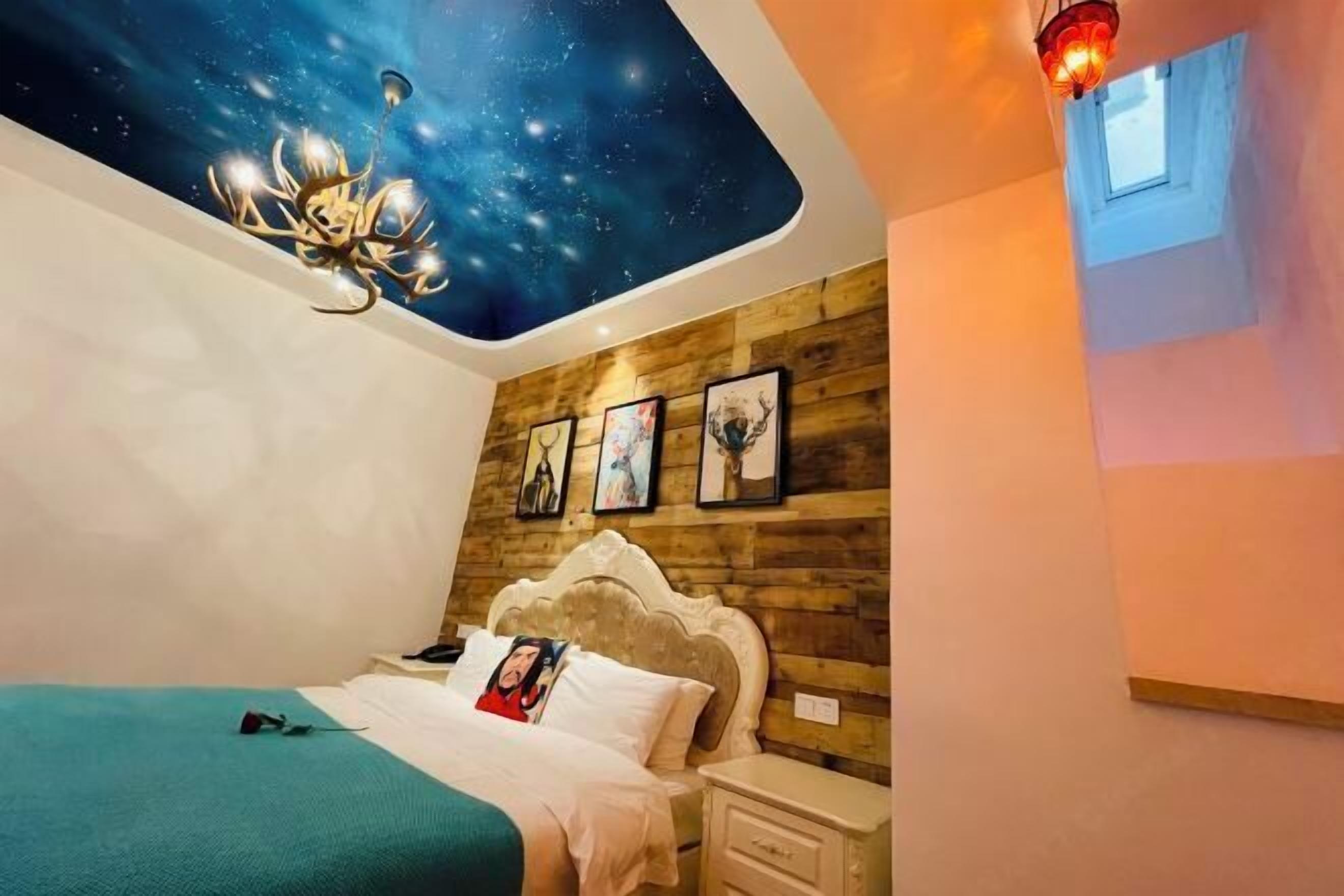 A bedroom with a starry sky ceiling, wooden panel wall, a bed with a headboard, bedside tables, and framed pictures.