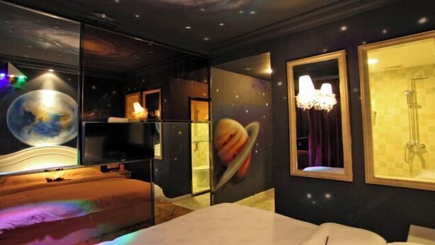 Una habitación con techo decorado con motivos galácticos, una cama, un televisor y una zona de ducha.