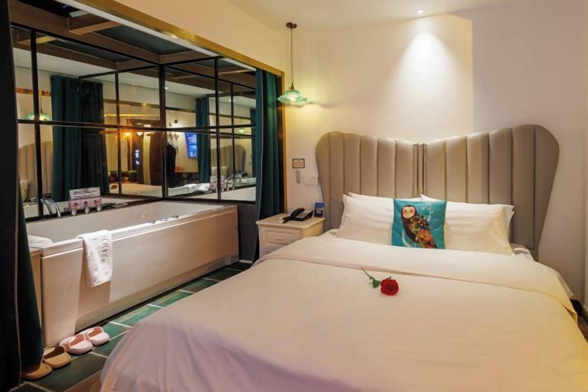 A hotel room with a large bed, a bathroom with a bathtub, a mirror, and a nightstand with a phone.