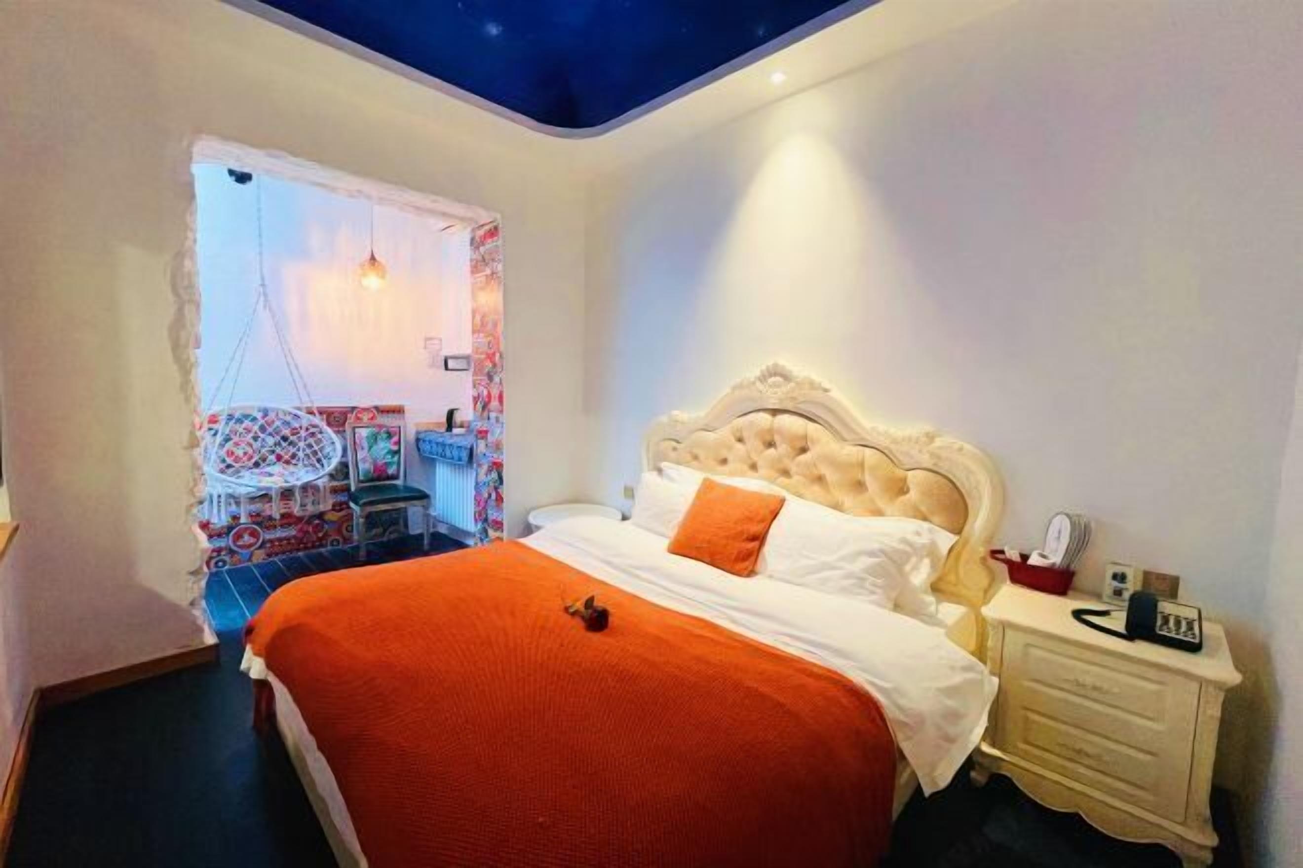 A bedroom with a large bed, a nightstand, a chair, and a ceiling with a starry design.