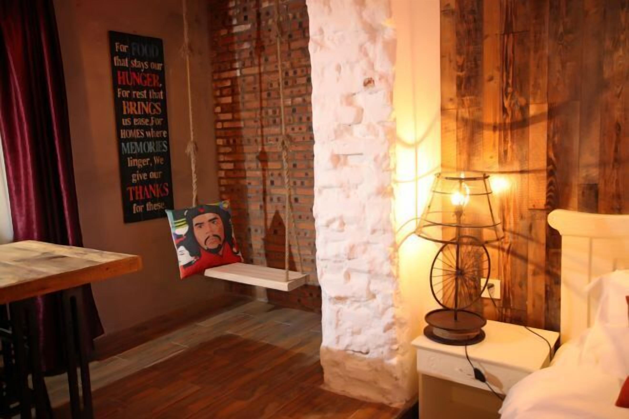 Une pièce chaleureuse avec un mur en briques, un plancher en bois, un lit blanc, une lampe suspendue et un tableau accroché au mur.