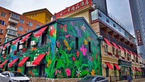 Un hotel con un mural colorido de flores tropicales en su fachada, varios balcones y un cartel que indica que es un hotel.