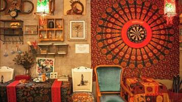 A room with a dartboard, a chair, a table with a patterned tablecloth, and various decorative items on shelves and the wall.