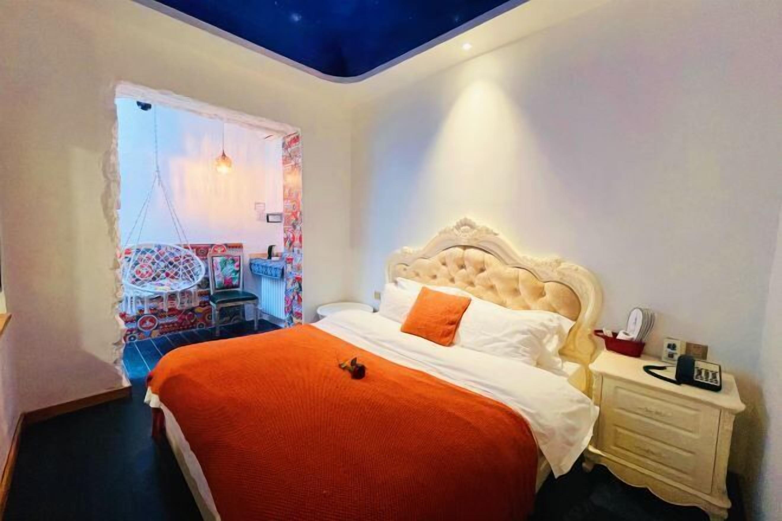 A bedroom with a large bed, a nightstand, a chair, and a ceiling with a starry design.