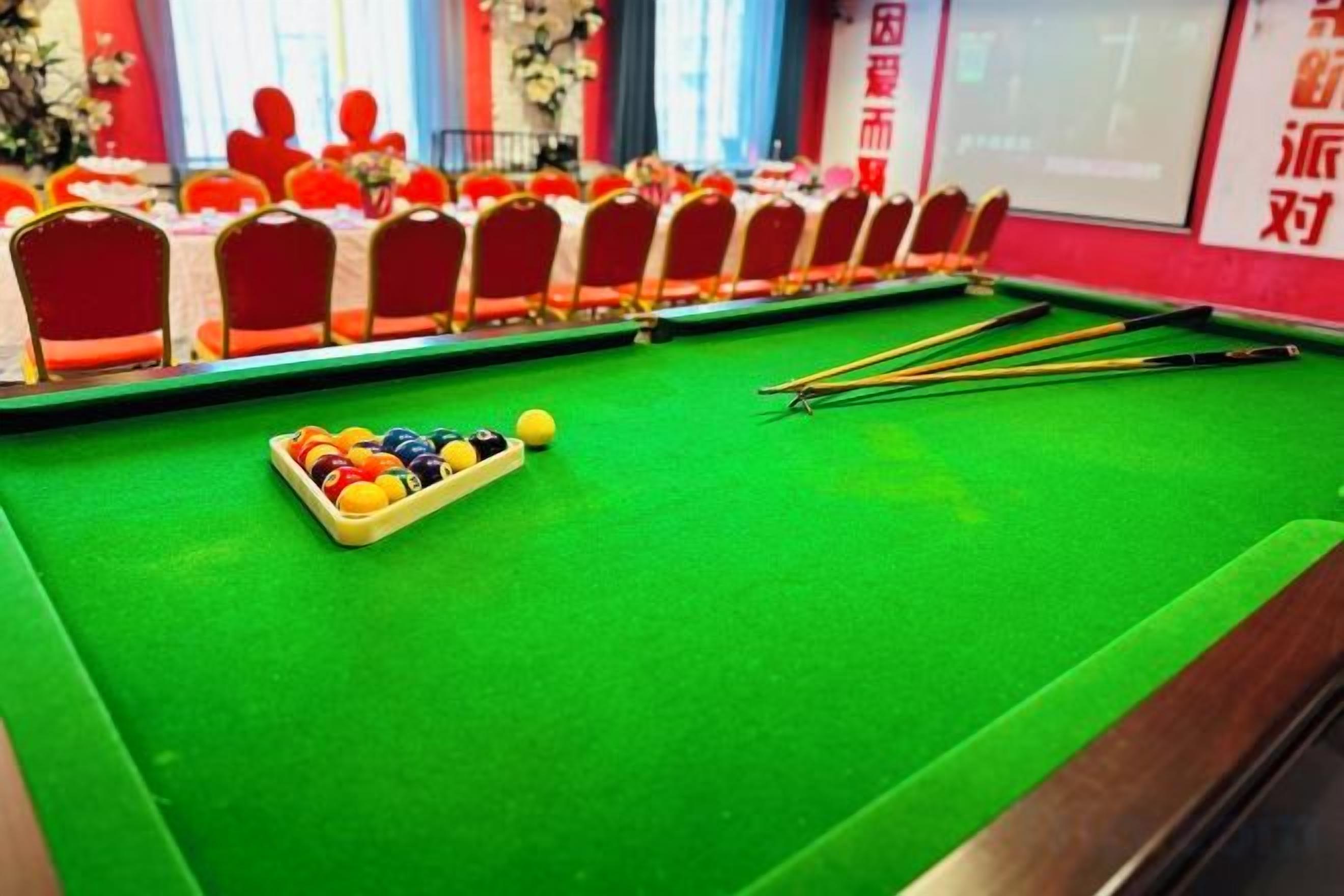 Ein Billardtisch mit Kugeln und Spielstöcken, umgeben von roten Stühlen.