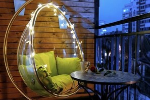 A hanging chair with cushions and string lights, a small round table with a cup and a book, and a balcony railing. - YDOO &YGOO Hotel (Shenyang)