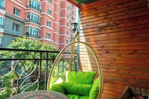 A hanging chair with a cushion, a wooden wall, and a balcony with a view of a red building.