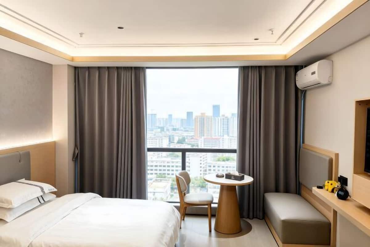 Une chambre d’hôtel comprenant un lit, un bureau, une chaise, une petite table et une grande fenêtre donnant sur la ville.