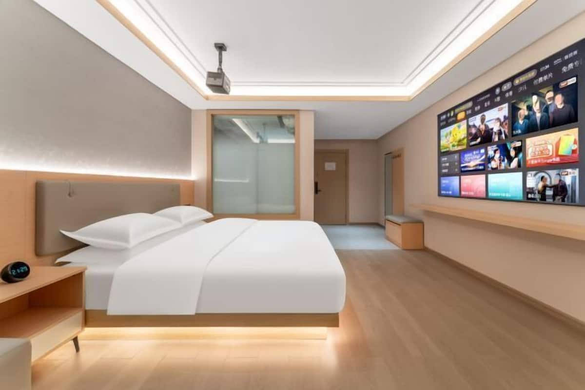 Une chambre d’hôtel moderne dotée d’un grand lit, d’une table de chevet, d’un mur entier dédié à la télévision et d’un projecteur au plafond.