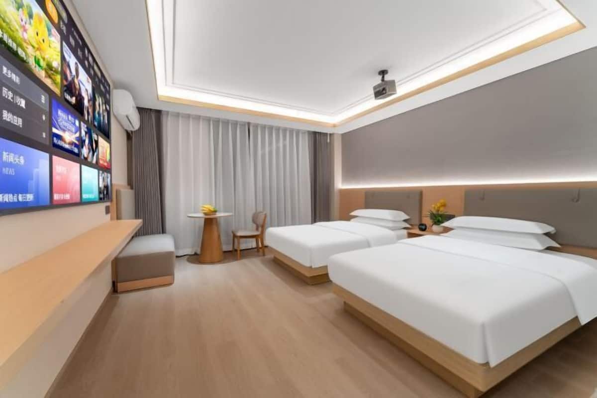 Une chambre d’hôtel moderne équipée de deux lits, d’un bureau, d’un téléviseur fixé au mur et d’un projecteur au plafond.