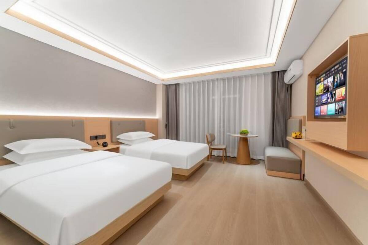 Une chambre d’hôtel moderne équipée de deux lits, d’un bureau, d’une chaise et d’un téléviseur fixé au mur.