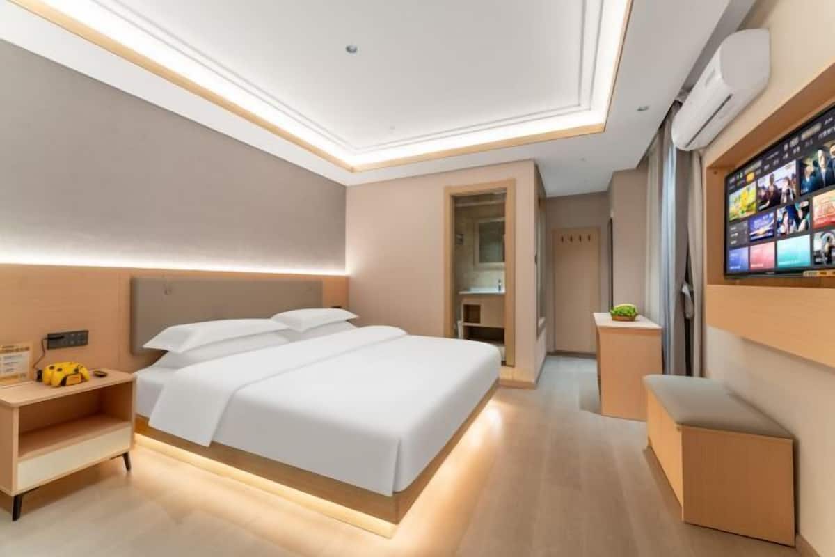 Une chambre d’hôtel moderne dotée d’un grand lit, de tables de chevet, d’un téléviseur fixé au mur et d’un dressing.