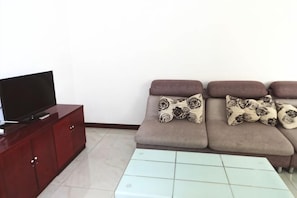 A living room with a sofa, a glass coffee table, a TV on a wooden cabinet, and patterned cushions. - Mihua Short Rent Apartment (Xi'an)