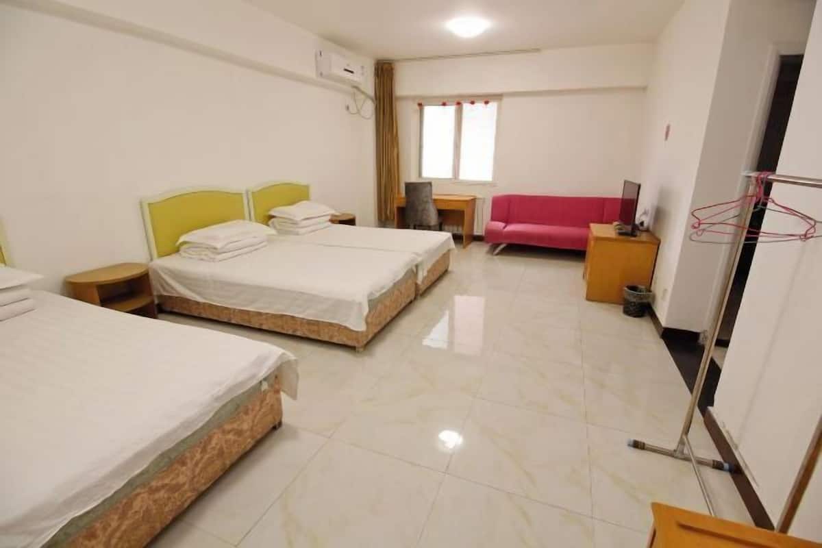 A hotel room with two beds, a desk, a chair, a red sofa, and a clothes drying rack.