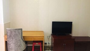 Een kamer met een houten bureau, een rode kruk, een televisie op een kast en een gestreept stoel.