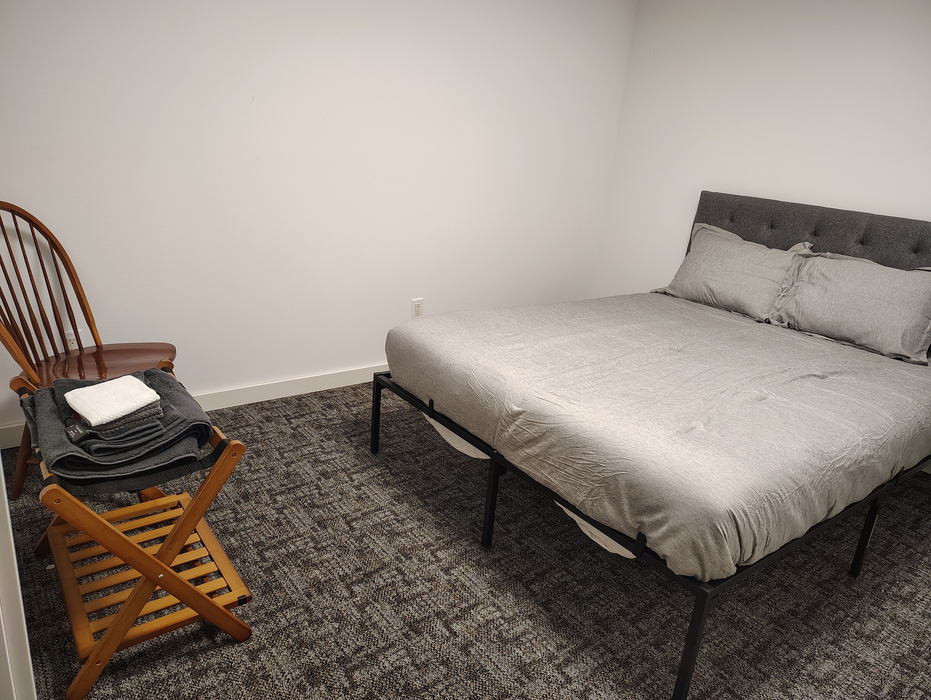 Ein Schlafzimmer mit einem Bett, einem Holzstuhl und einem kleinen Tisch mit einer zusammengefalteten Decke und einem Buch.