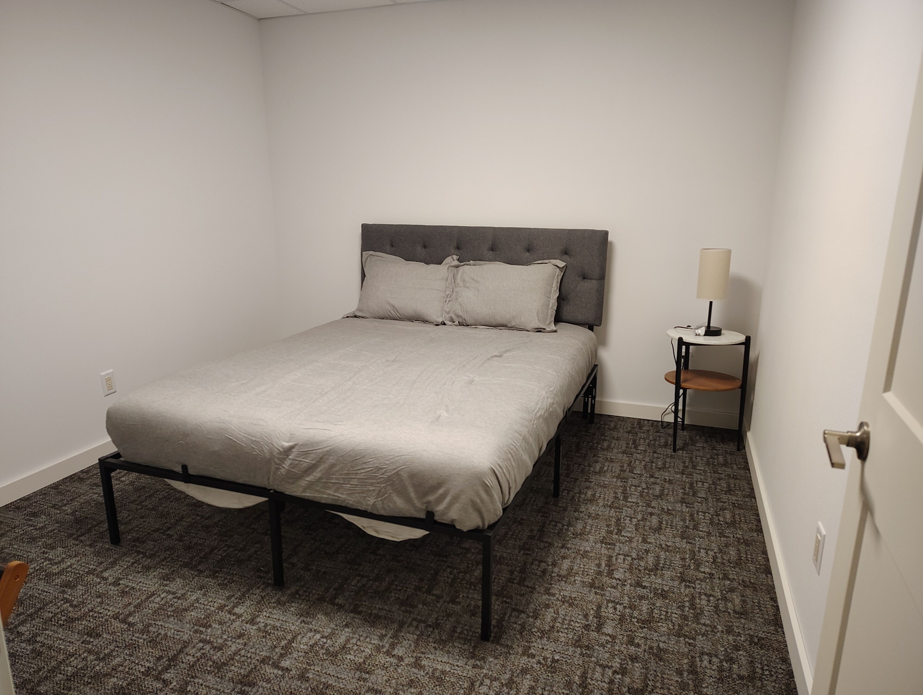 A bedroom with a bed, a nightstand, a lamp, and a chair.