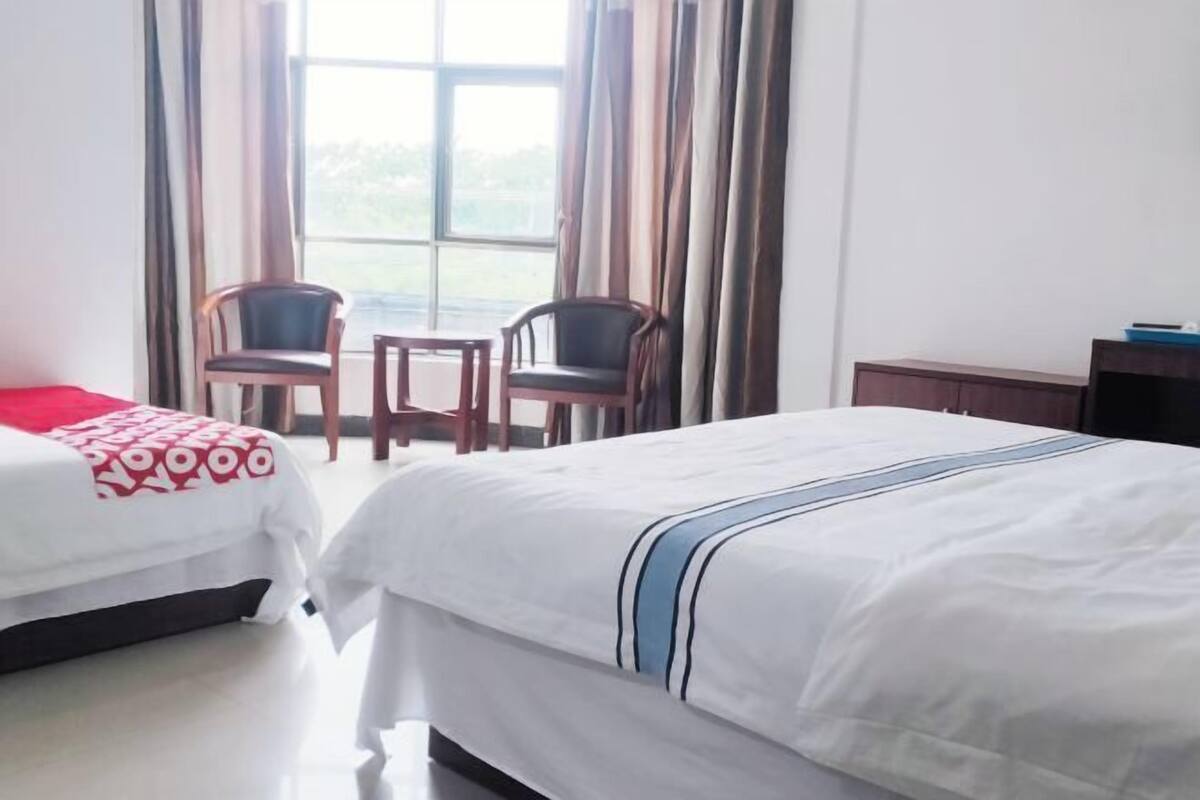 Een hotelkamer met twee bedden, een tafeltje, twee stoelen en een raam met gordijnen.
