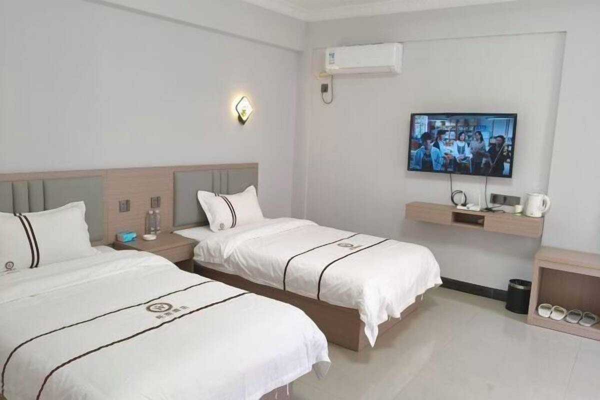 Een hotelkamer met twee bedden, een televisie, een plank met een waterkoker en een schoenenrek.
