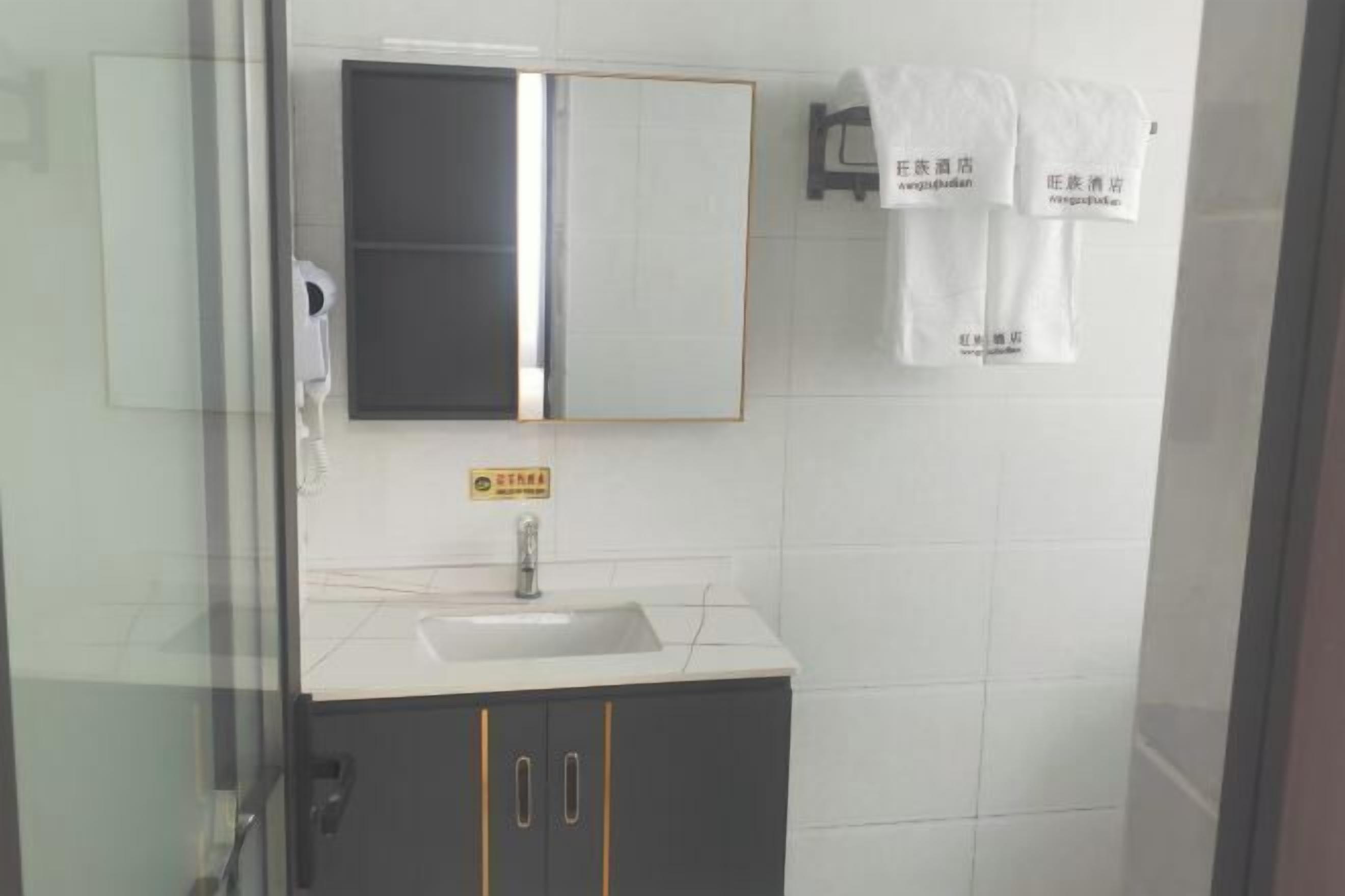 Un baño con lavamanos blanco, espejo y toallero con toallas.
