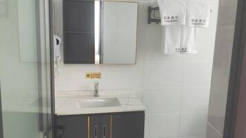 Un baño con lavamanos blanco, espejo y toallero con toallas.