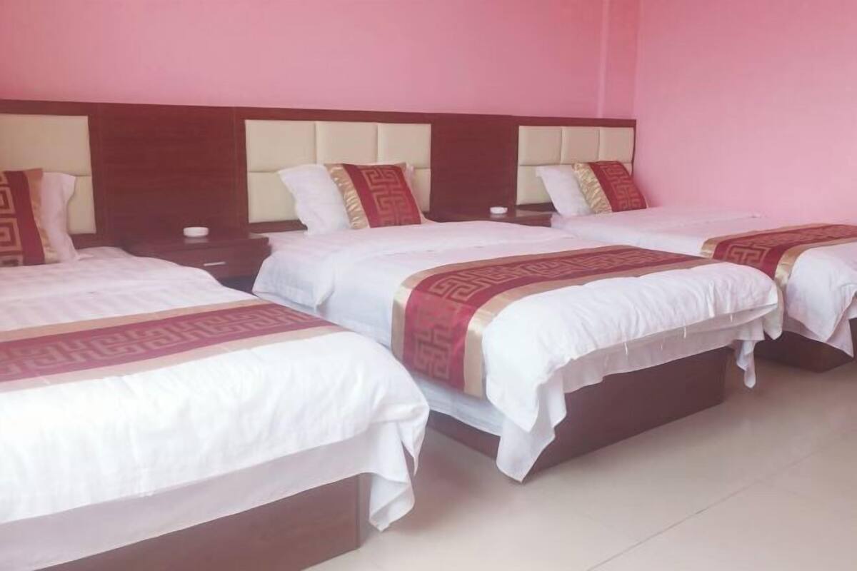 Een hotelkamer met drie bedden, elk voorzien van witte lakens en rode sierkussens.