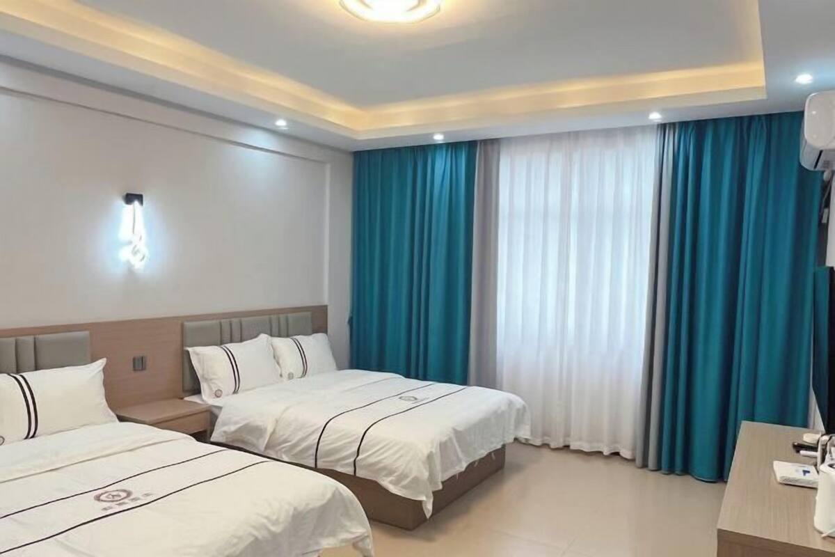 Een hotelkamer met twee bedden, een bureau en een groot raam met gordijnen.