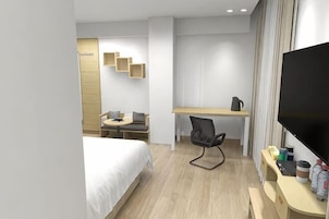Habitación de hotel con cama, escritorio, silla, televisor y un pequeño rincón de descanso con mesa y sillas.