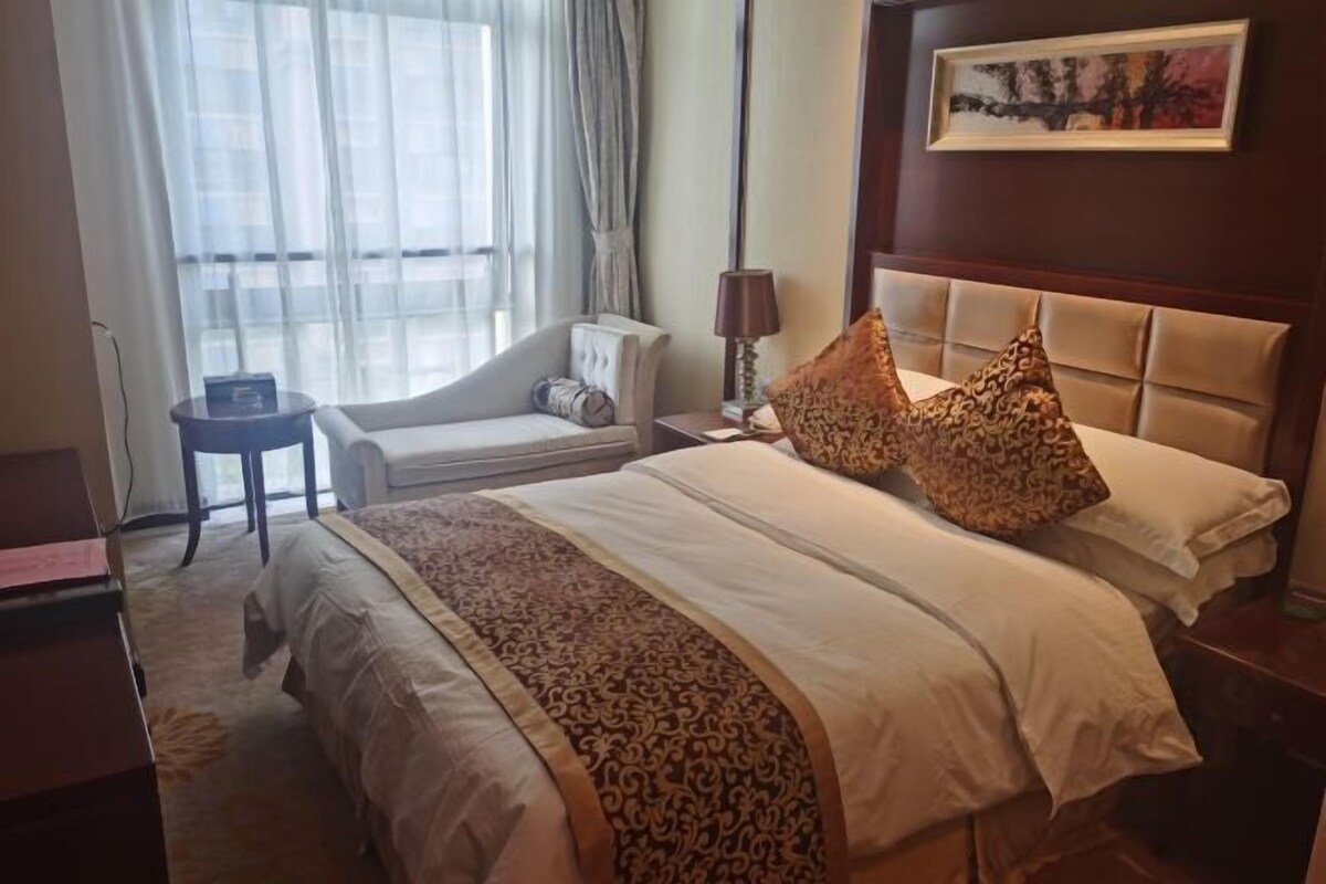 A hotel room with a bed, a chair, a lamp, and a painting on the wall.