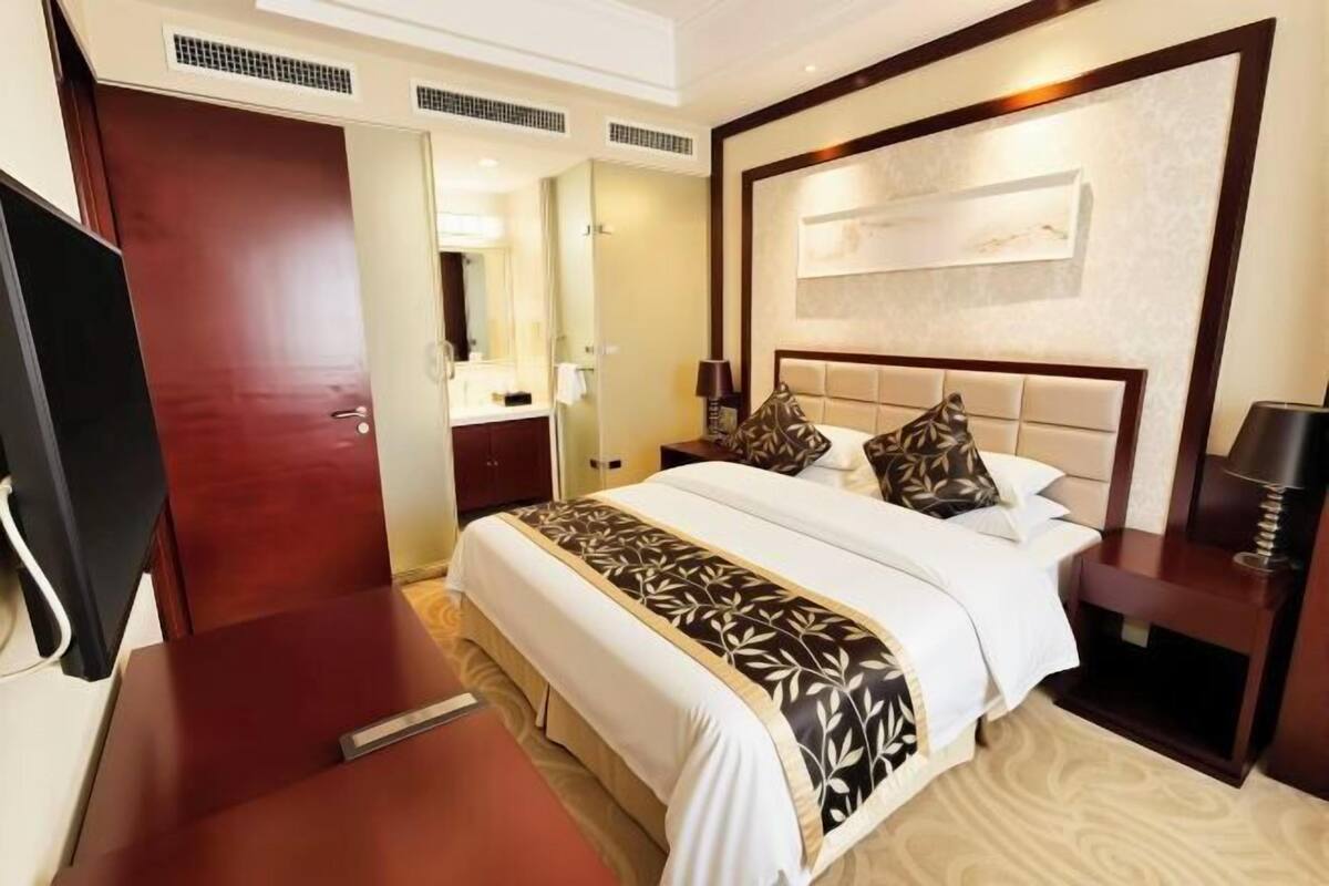 Una habitación de hotel con cama, mesita de noche, lámpara y televisor.
