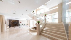 Eine geräumige Lobby mit einer zentralen Treppe, einem Empfangsbereich und Zimmerpflanzen.