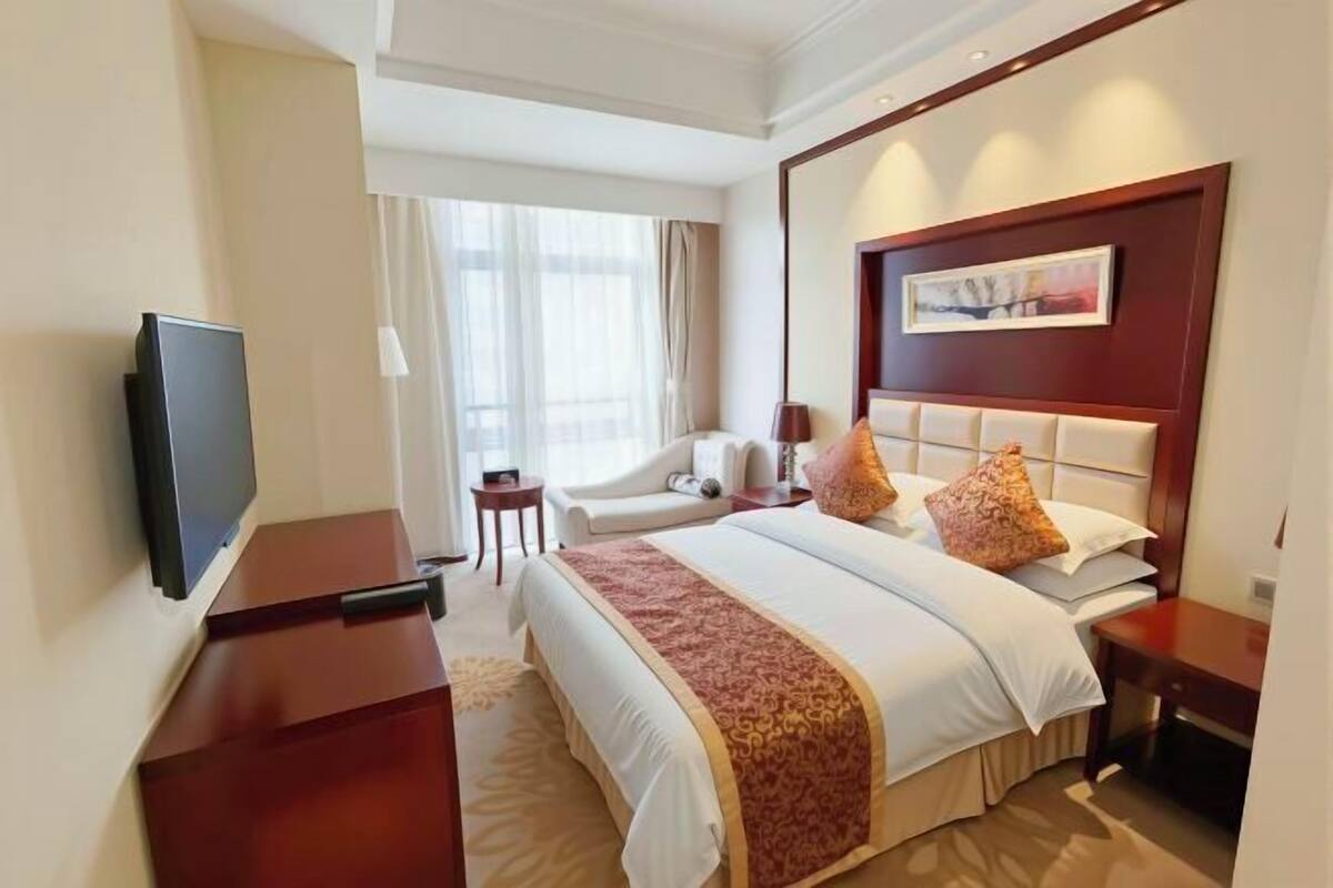 Una habitación de hotel con una cama grande, televisión, escritorio y una silla.