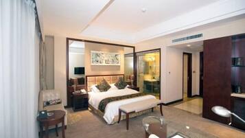 A hotel room with a large bed, a desk, a chair, a sofa, and a glass partition.