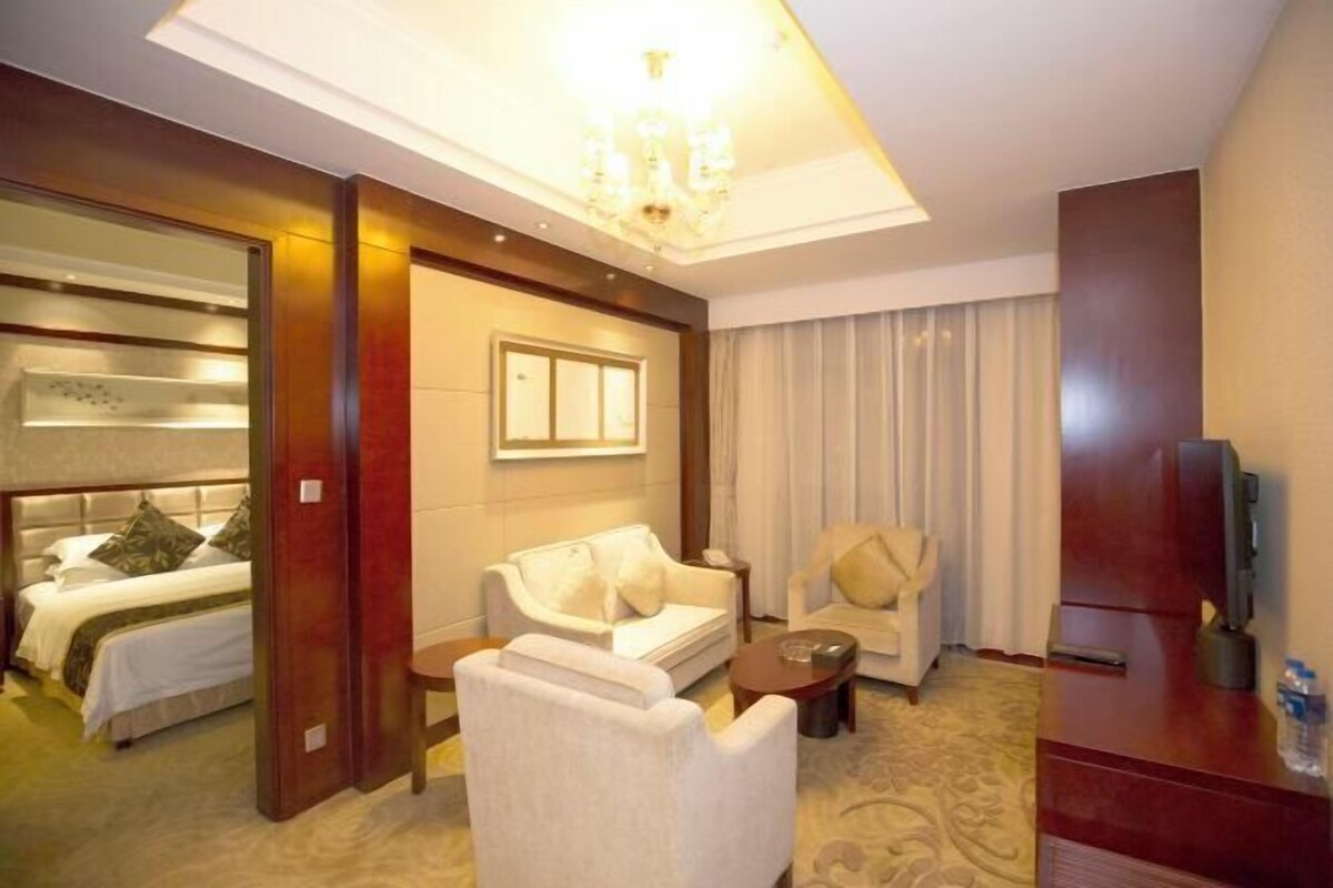 A hotel room with a bed, two white sofas, a small table, a TV, and a chandelier.