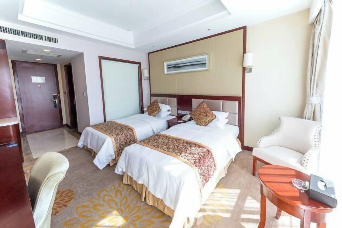 A hotel room with two beds, a desk, a chair, and a sofa.